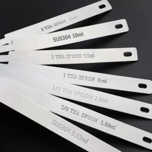 ZEST seven stainless steel measuring spoon handles engraved 0.63ml to 15ml fanned out on a black background