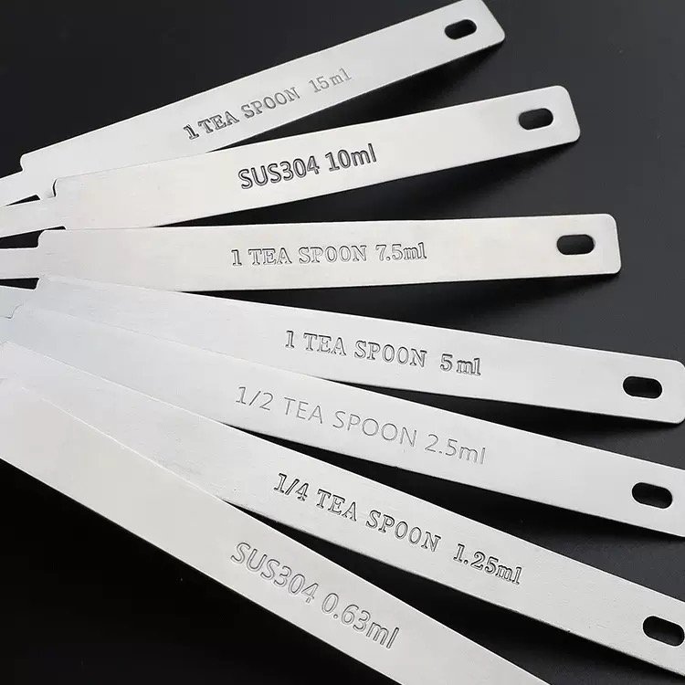 ZEST seven stainless steel measuring spoon handles engraved 0.63ml to 15ml fanned out on a black background