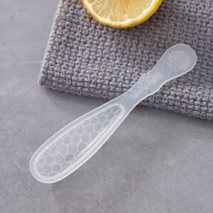 ZEST translucent plastic honey spoon with a honeycomb-pattern head beside a lemon slice on grey cloth
