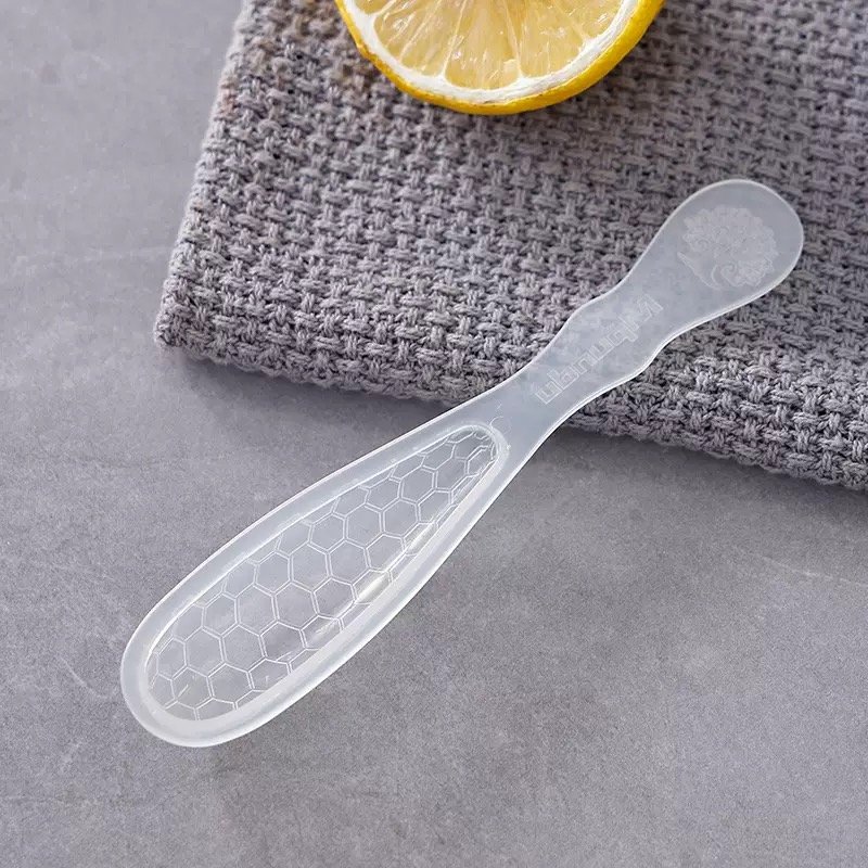 ZEST translucent plastic honey spoon with a honeycomb-pattern head beside a lemon slice on grey cloth
