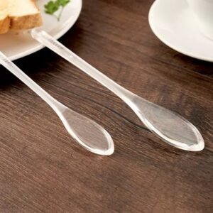 ZEST clear plastic honey dipper stick spoons with flat leaf-shaped heads on a wooden table beside breakfast toast